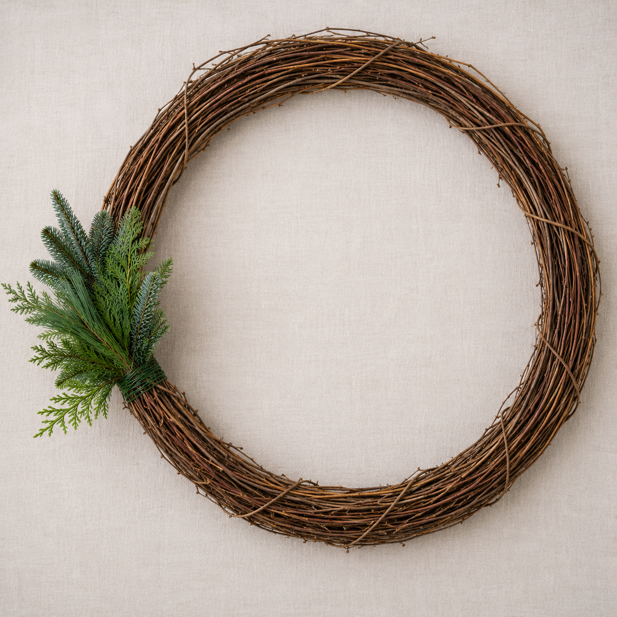 Small bundle of mixed evergreen branches attached to a willow wreath base, showing the first step in creating a Christmas wreath.