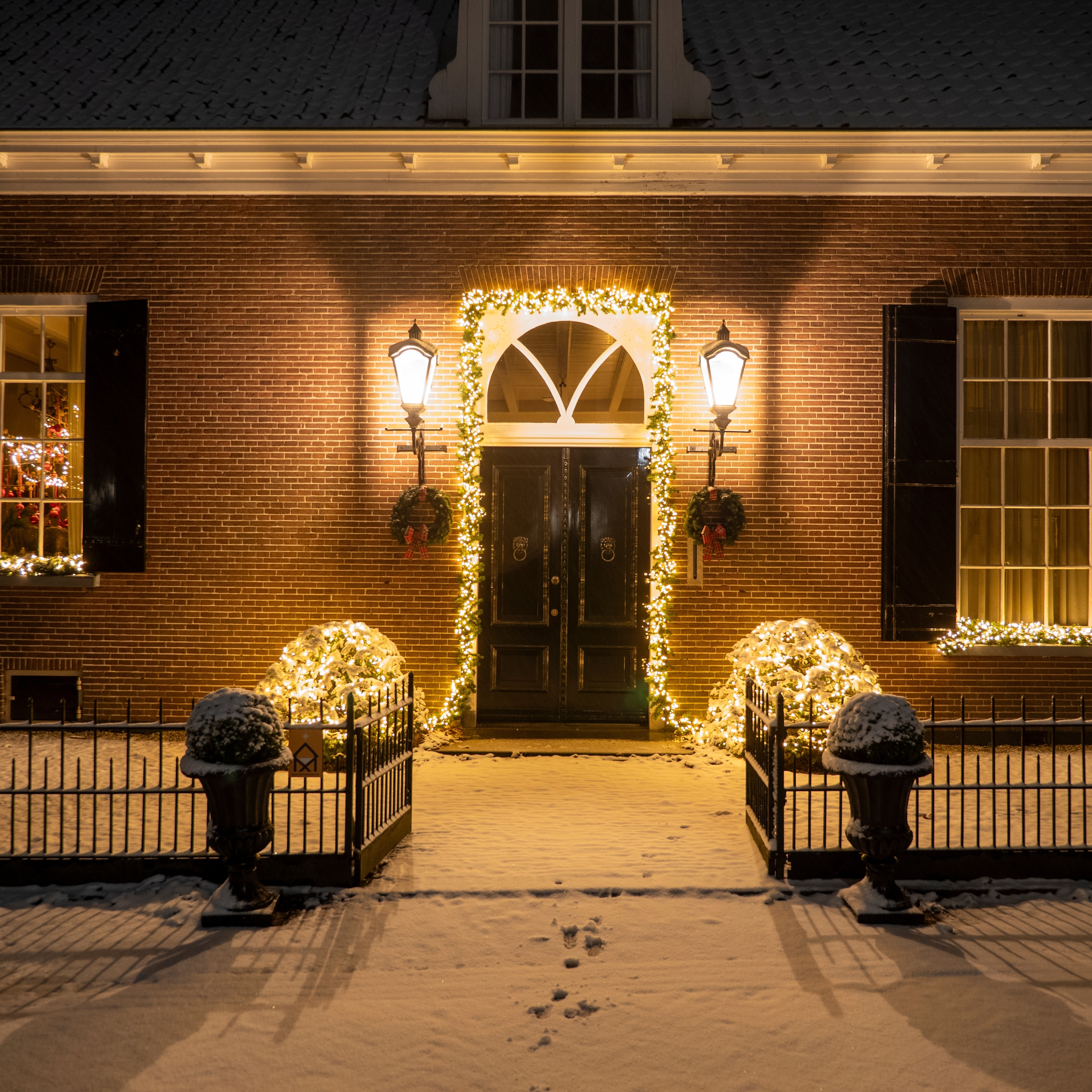 House entrance decorated with outdoor Christmas lighting, illuminated garlands and wreaths creating a welcoming festive display.