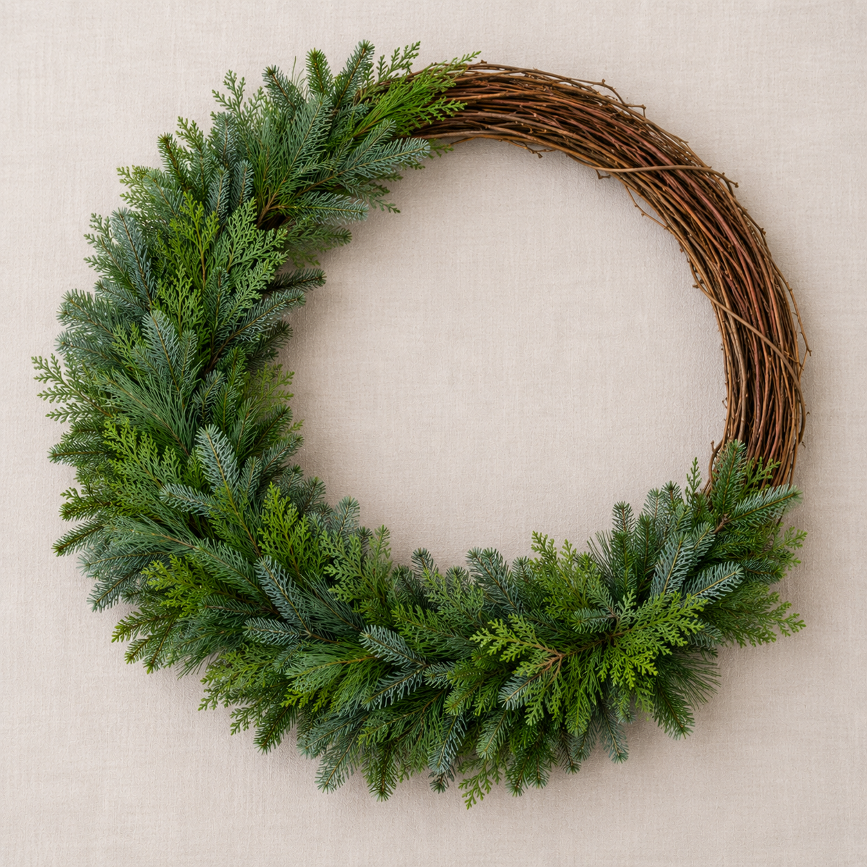 Evergreen bundles layered around a willow wreath base, showing how overlapping greenery creates a full, textured Christmas wreath.