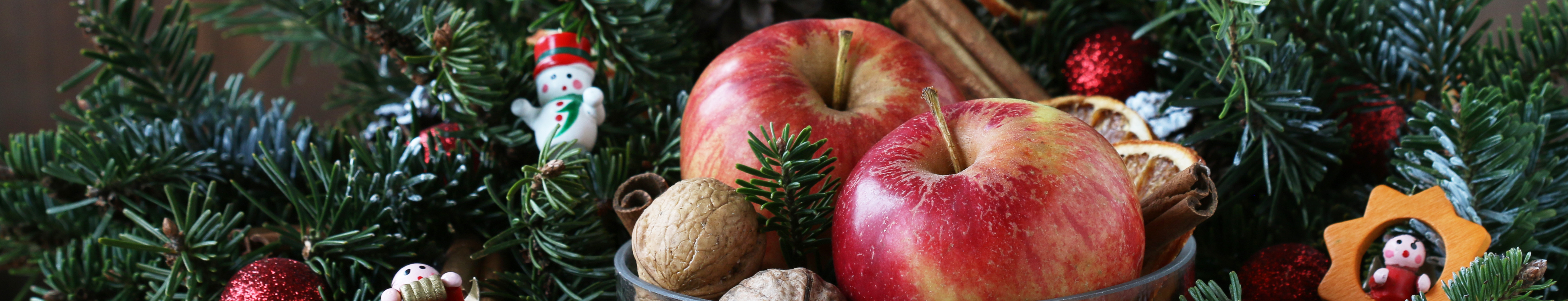 Natural Christmas table decoration with evergreen foliage, apples and nuts, creating a festive seasonal centrepiece.