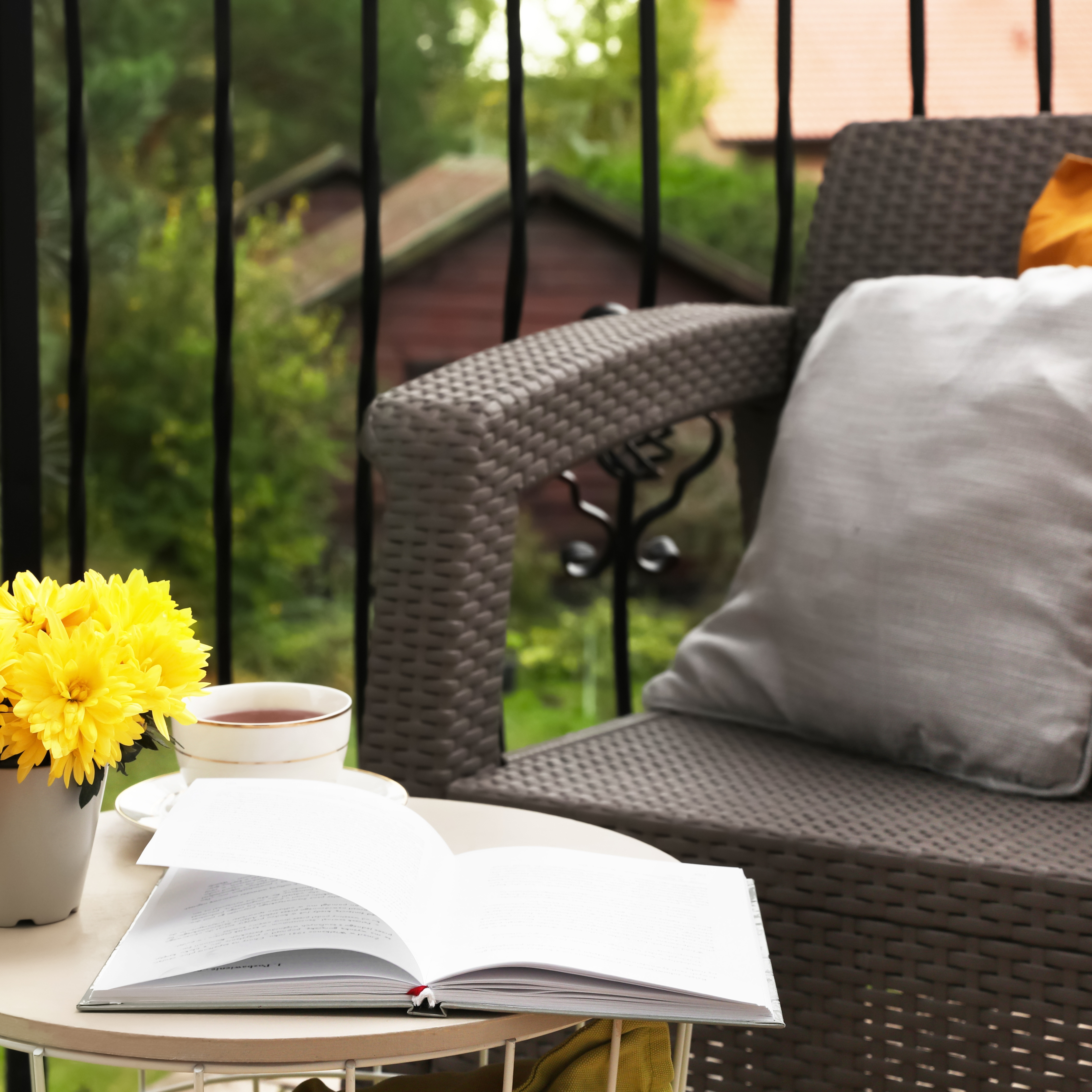 Garden chair with cushions beside a small table with flowers, a drink, and a book in a peaceful garden setting.