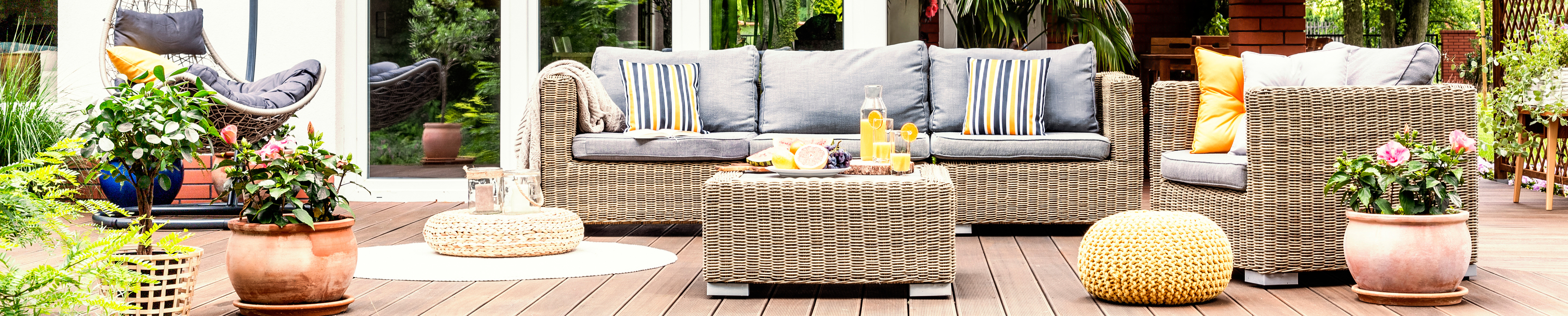 Comfortable outdoor living area with wicker patio furniture, potted plants and a timber deck